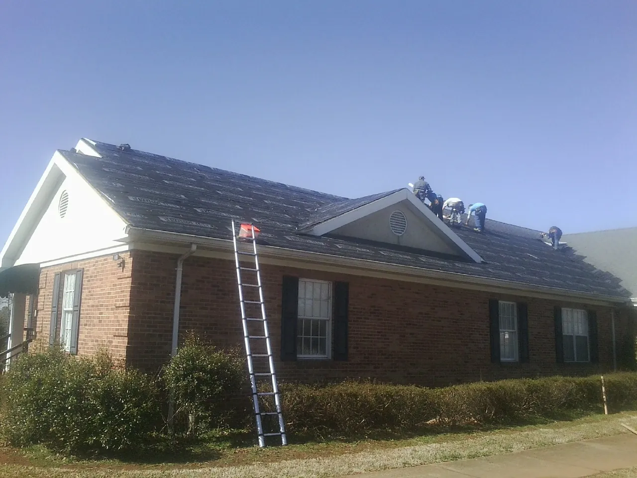 Crew tearing shingles off a brick ranch roof with a ladder set — Emergency Roof Repair work by our crew in Crosby