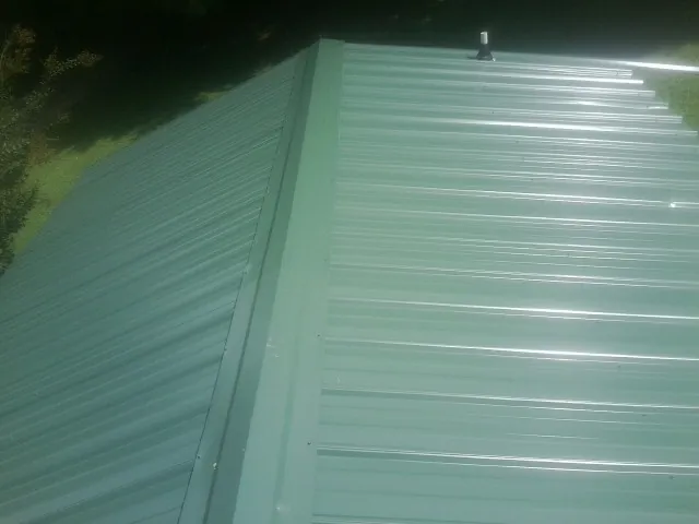 New green metal panels meeting at the ridge of a roof — Flat Roof Repair work by our crew in Crosby