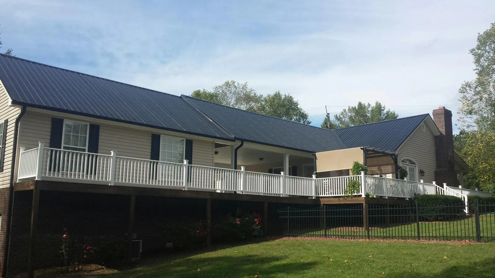 Black metal roof above a long white railed deck on a hillside home in Crosby