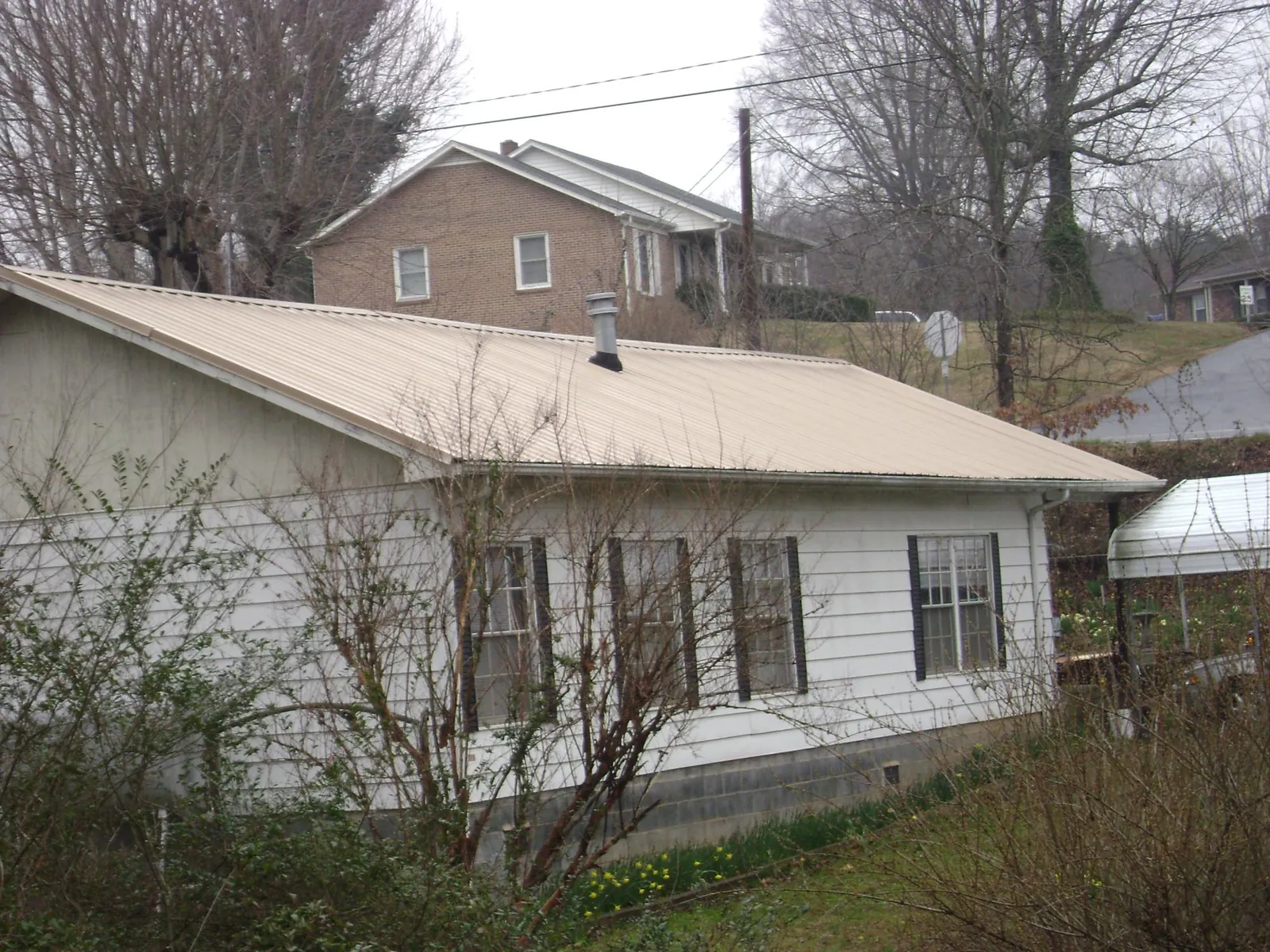 Tan metal roof on a white sided house set into a hillside — Commercial Roofing by Roofing Brothers in Crosby